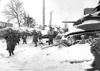American soldiers of the 117th Infantry Regiment, Tennessee National Guard, part of the 30th Infantry Division, move past a destroyed American M5 "Stuart" tank on their march to recapture the town of St. Vith during the Battle of the Bulge in January 1945. (Wiki)