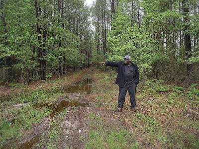 Carnelious Jones stands in the wooded 100-acre property on Hooper’s Island where the hatchery will go. It’s some of the highest ground on the low-lying island. (Dave Harp)